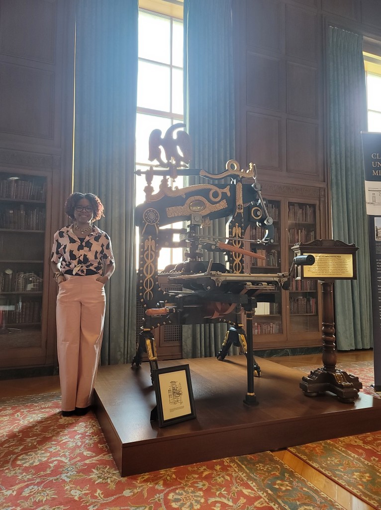 Teanu Reid in front of a printing press at the William L. Clements Library, University of Michigan